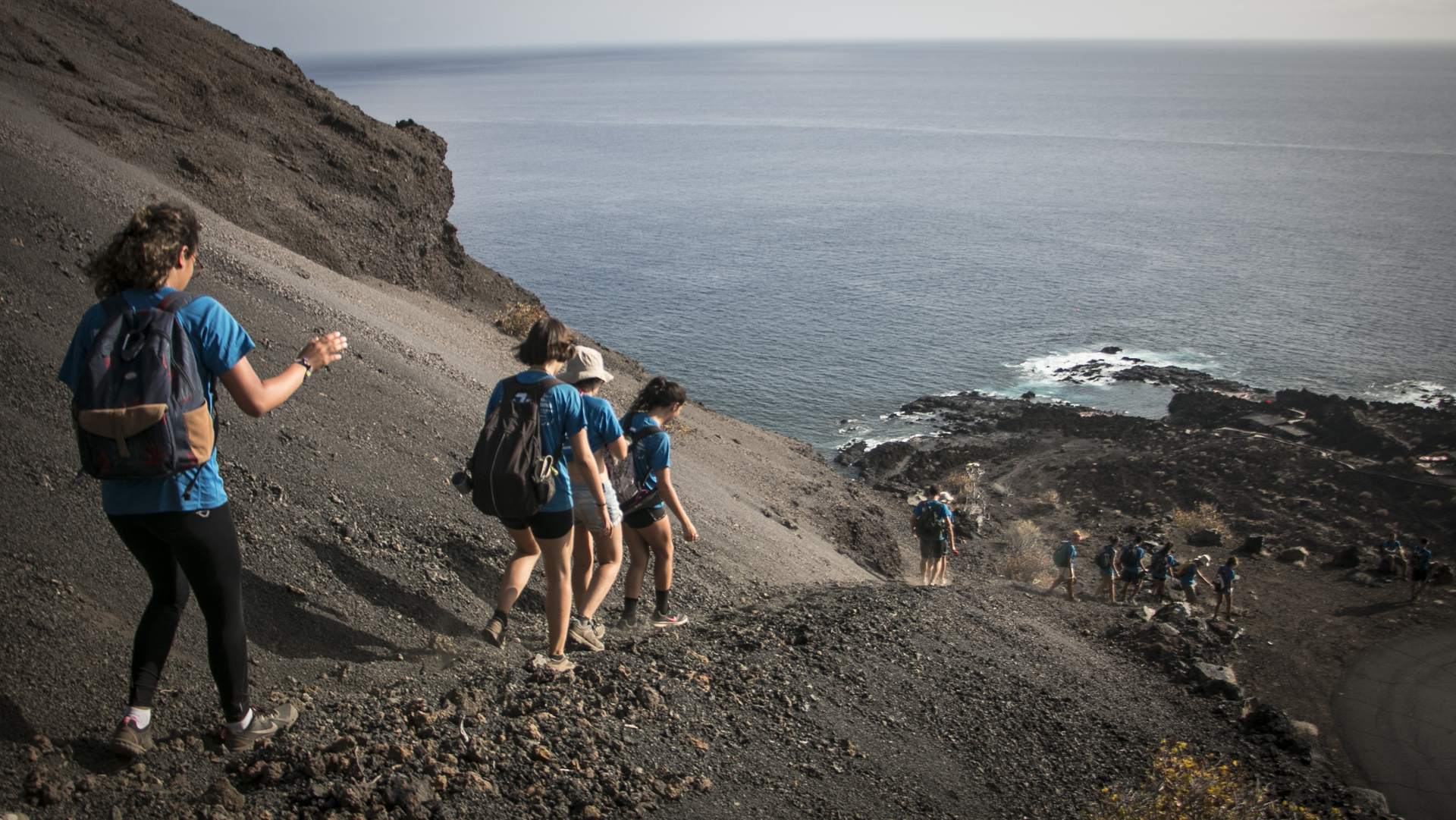 Grupo de Ruta Siete con mochilas bajando una ladera volcánica hacia el mar en Tacorón, El Hierro