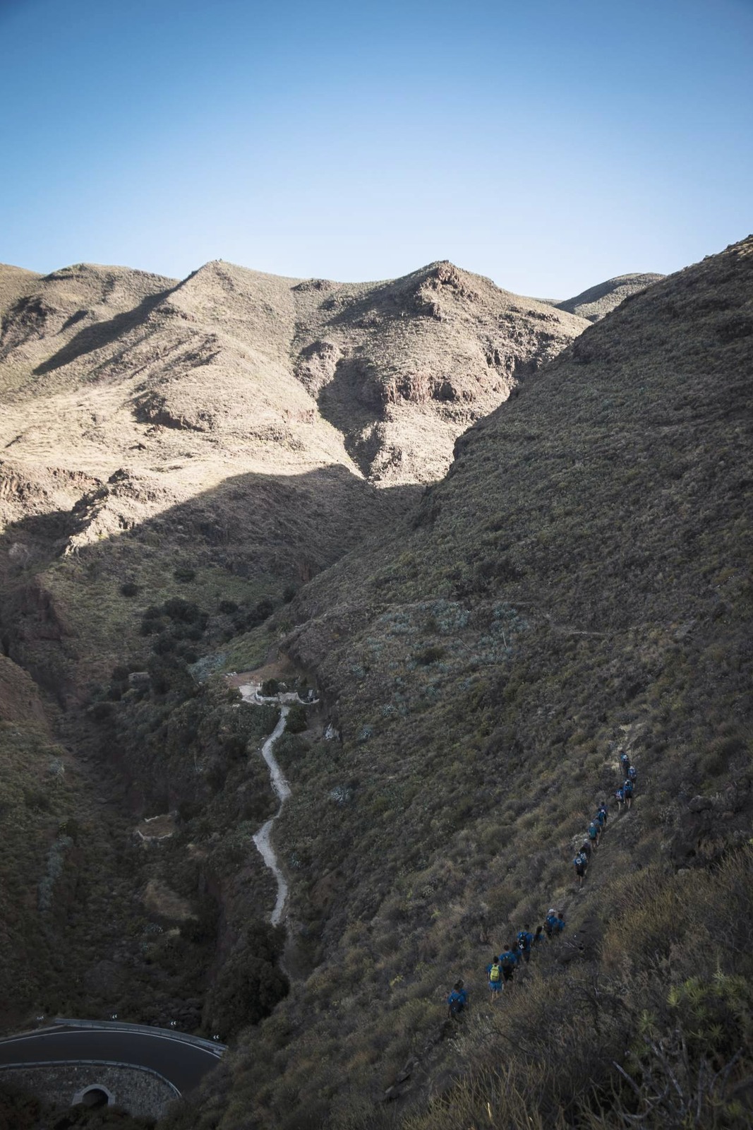 Grupo de senderistas en fila descendiendo un barranco de montaña en Gran Canaria, vistos desde lejos