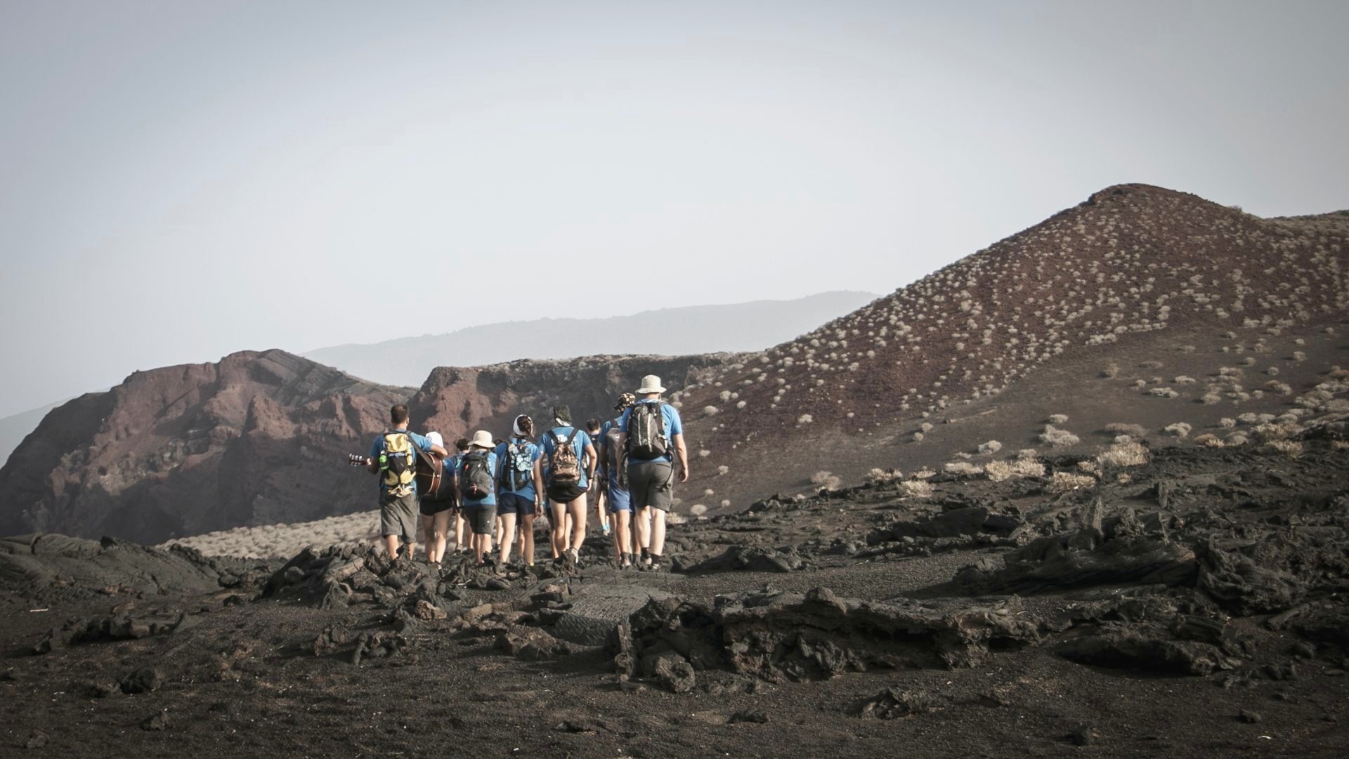 Grupo de Ruta Siete caminando en fila por un sendero volcánico de El Hierro, con el mar de bruma al fondo