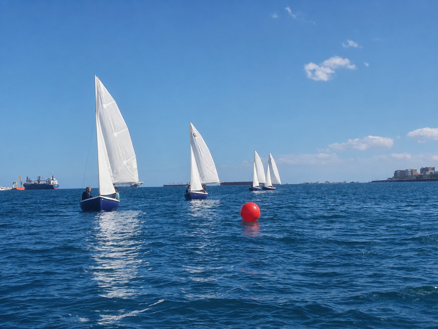 Veleros de una clase de vela navegando frente a la costa