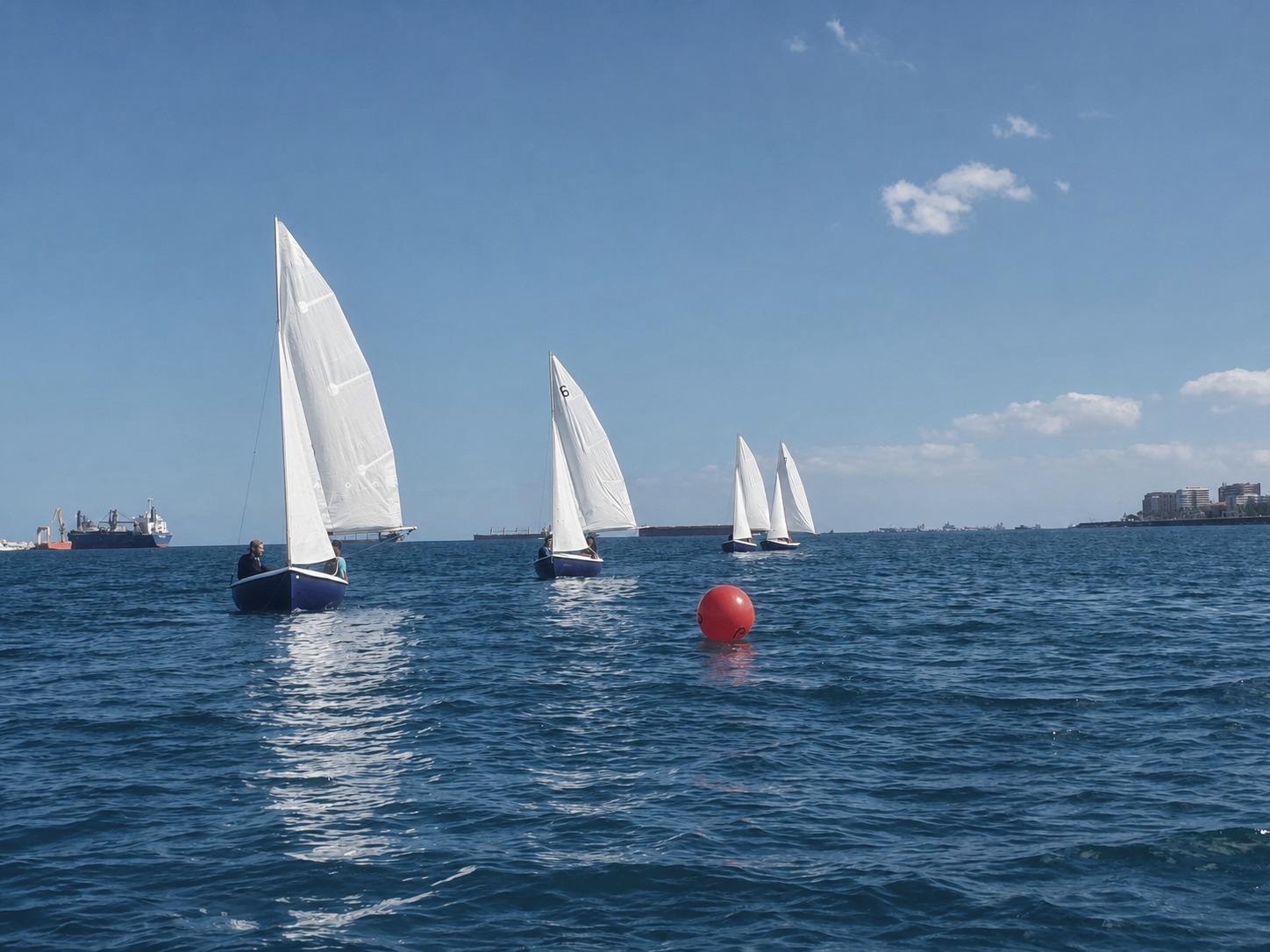 Veleros de una clase de vela navegando frente a la costa