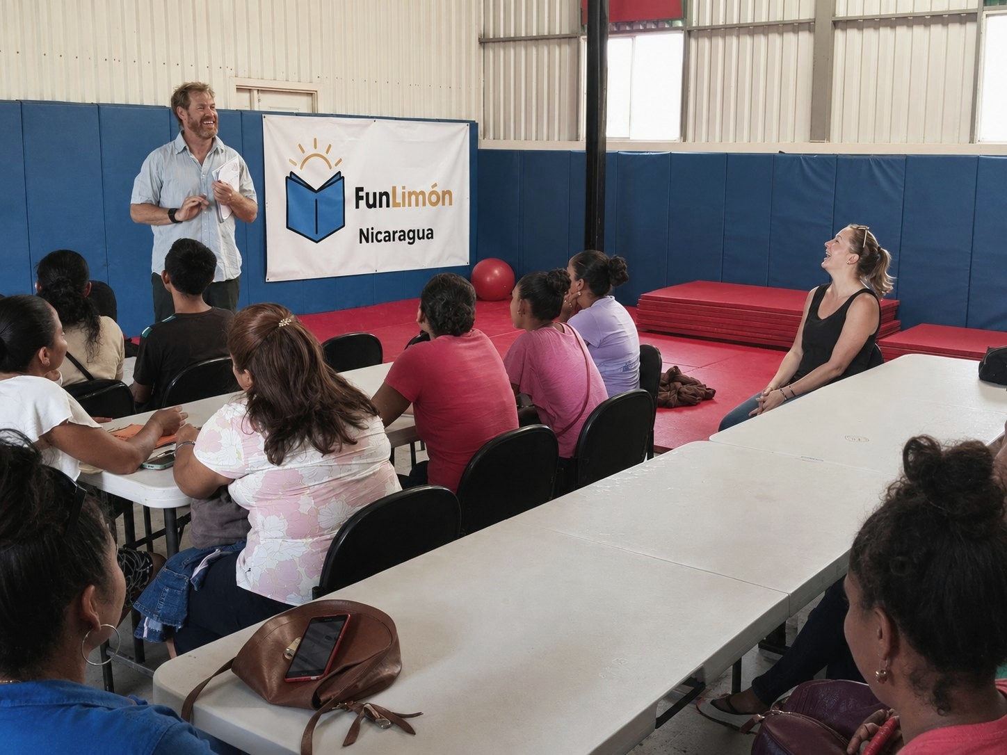 Juan Serantes hablando ante un grupo de mujeres en el gimnasio de FunLimón, Nicaragua, con el cartel FunLimón detrás