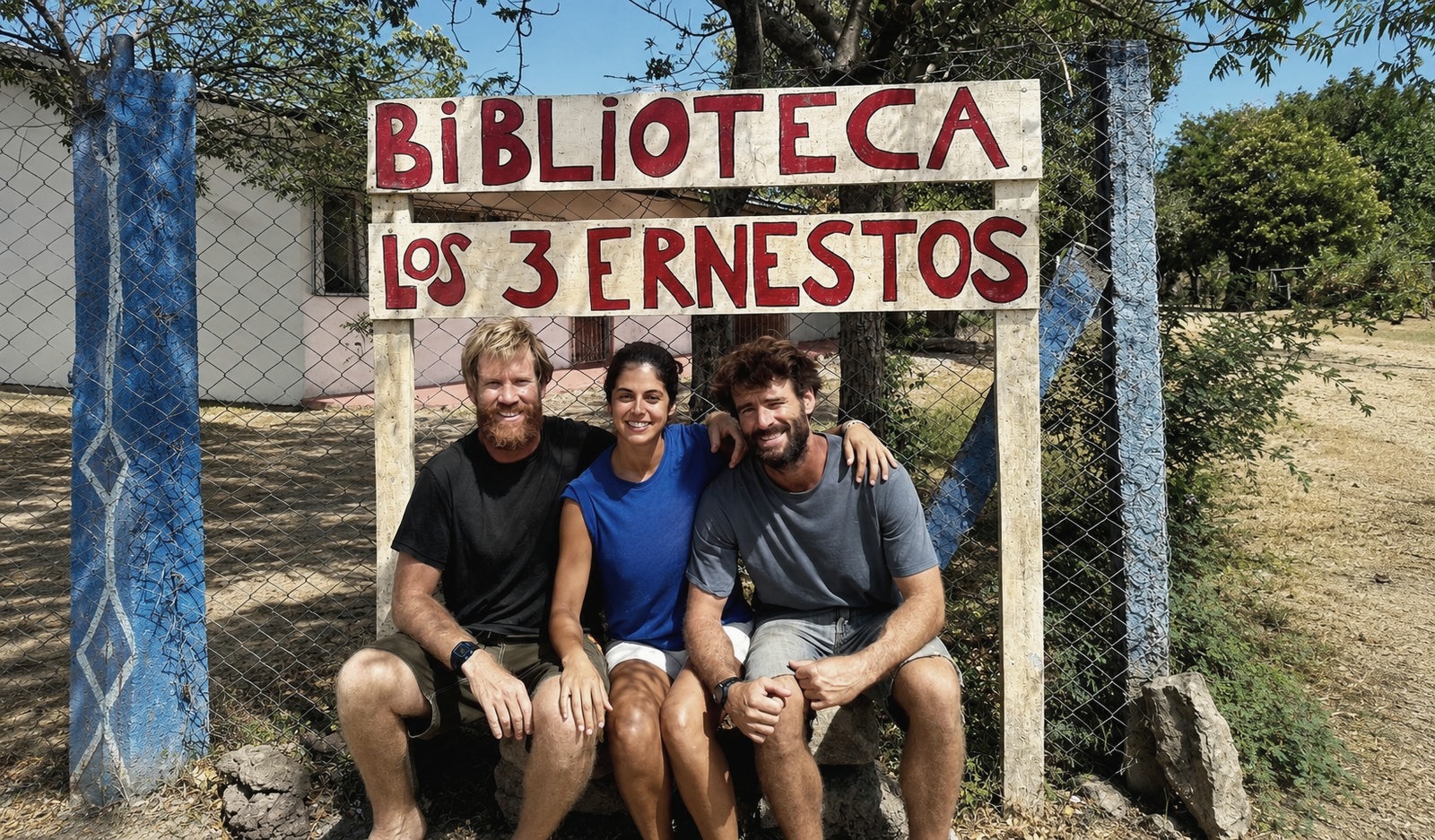 Juan Serantes con dos personas más bajo el cartel de la Biblioteca Los 3 Ernestos, en Nicaragua